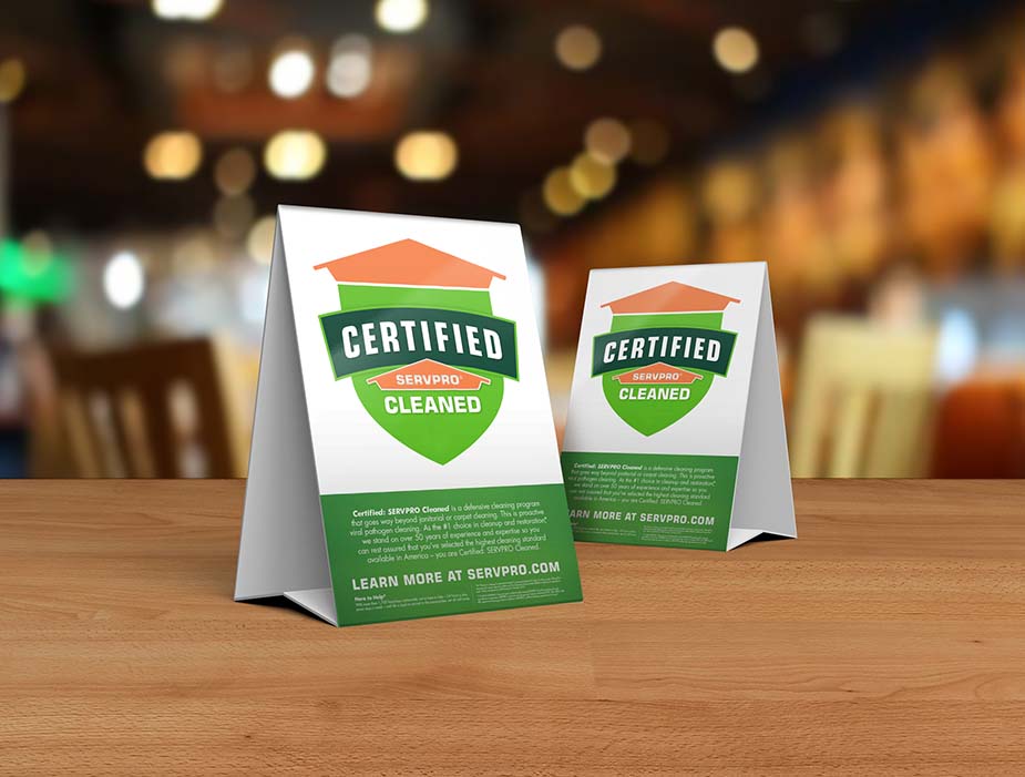 Table tent signs describing the Certified: SERVPRO Cleaned program on top of a wooden table